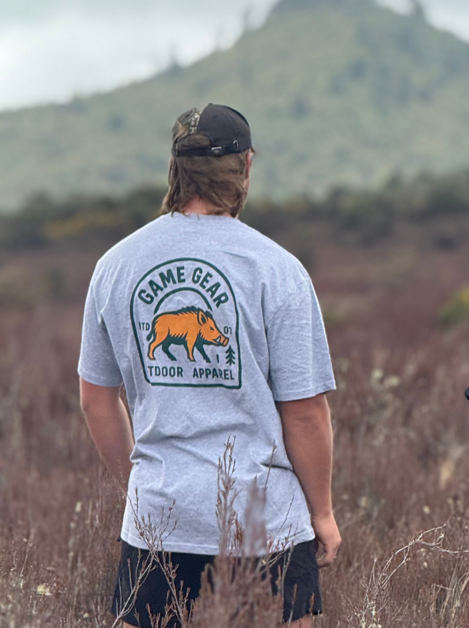 Person wearing a gray 'Game Gear Outdoor Apparel' t-shirt in a natural setting